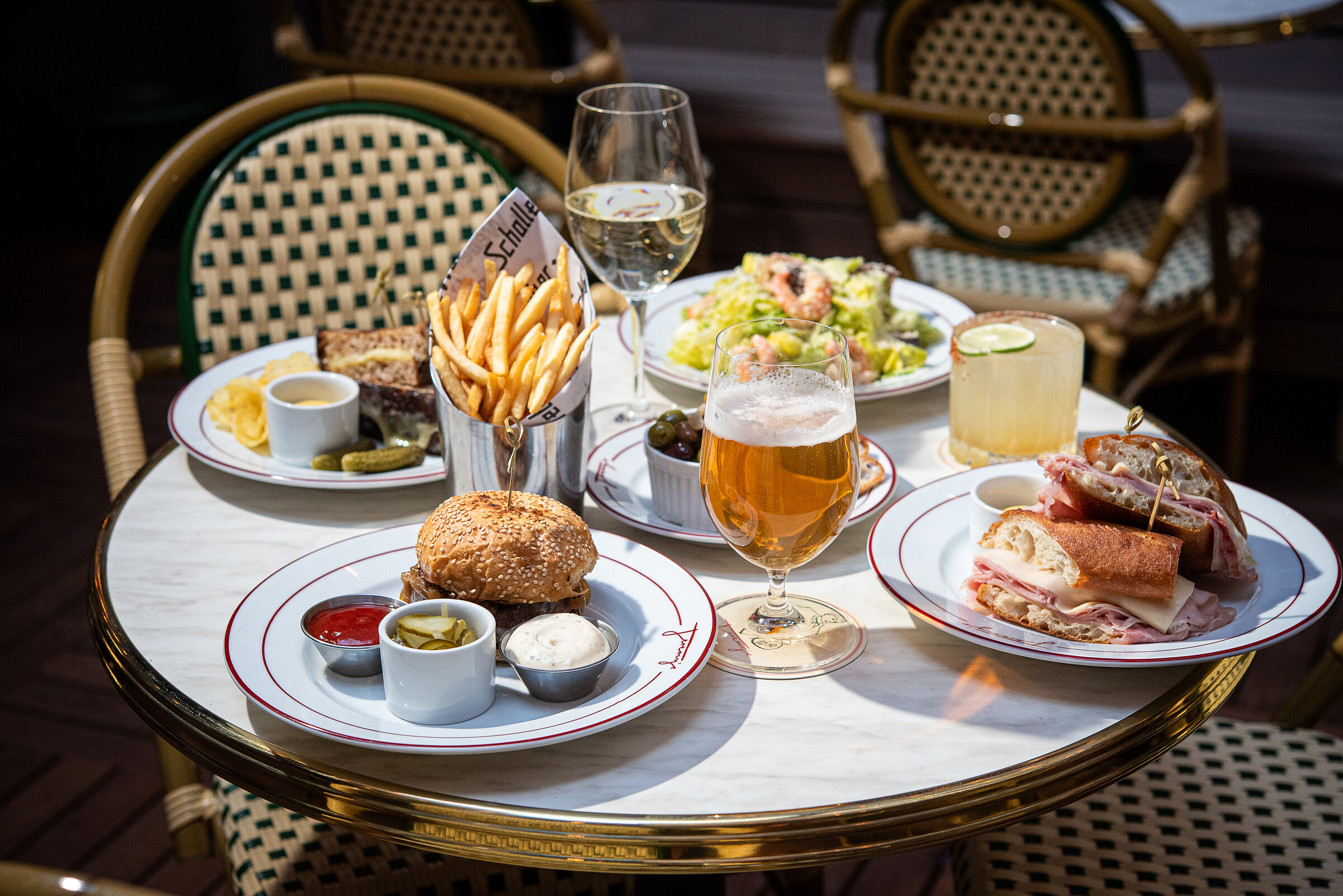 Patio dining spread — burger, salad, sandwich, olives, cocktails